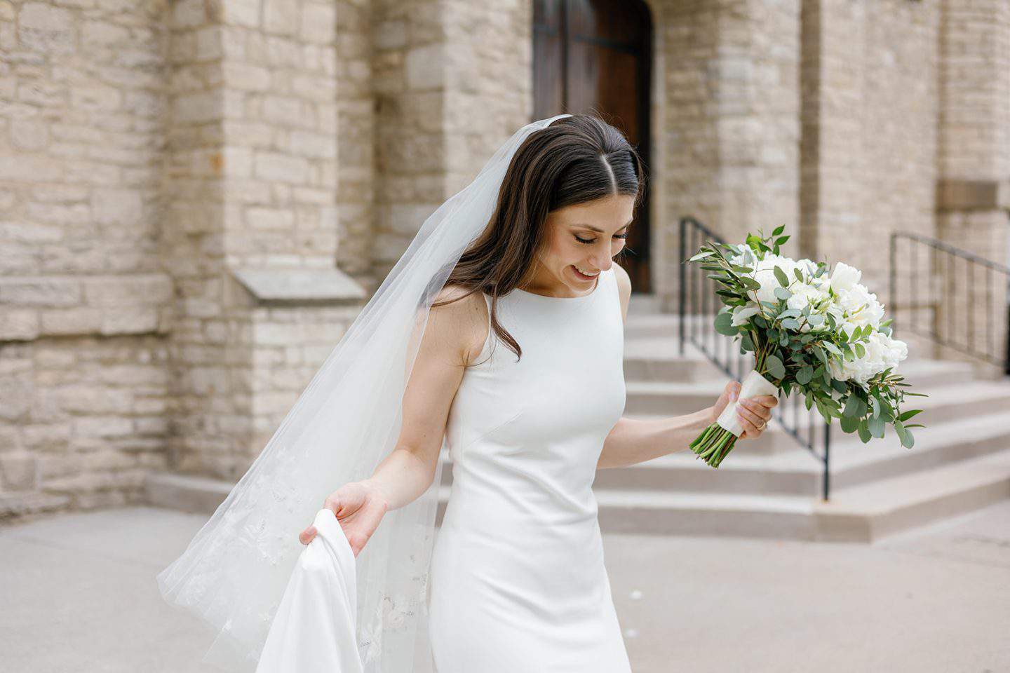 Candid wedding portrait of bride holding flowers outside church in Detroit.